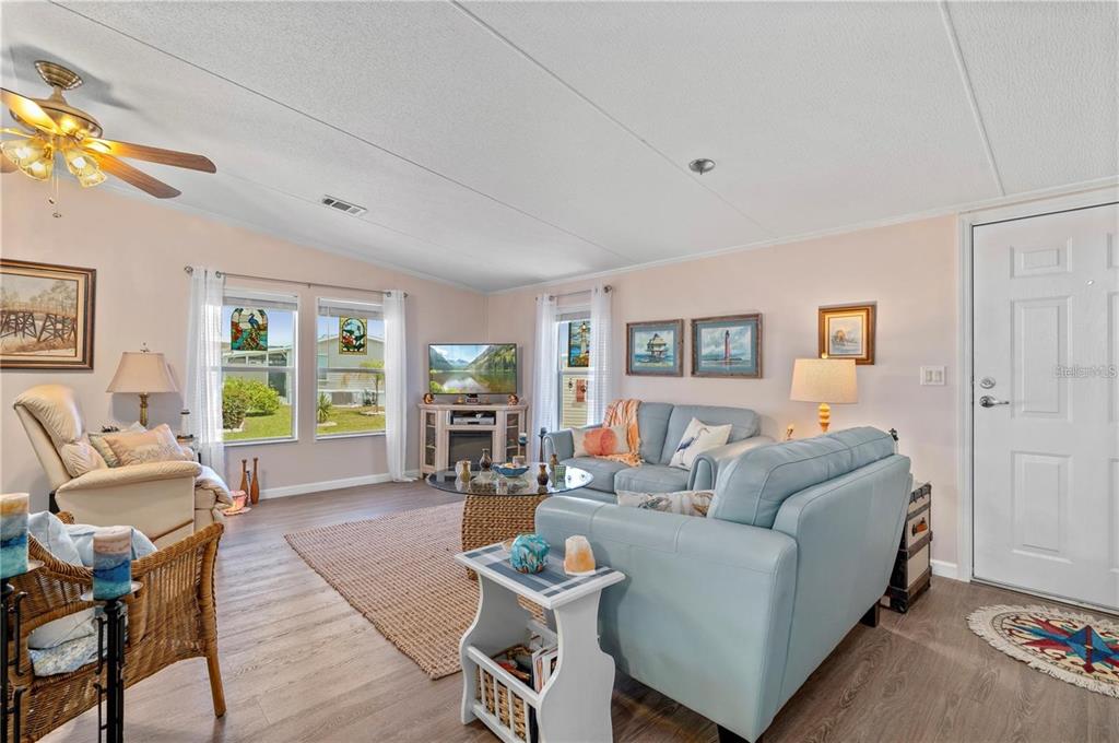 A living room features light wood-look flooring, a blue sofa, and a ceiling fan — 1000 KINGS HIGHWAY UNIT 133, PUNTA GORDA, FL