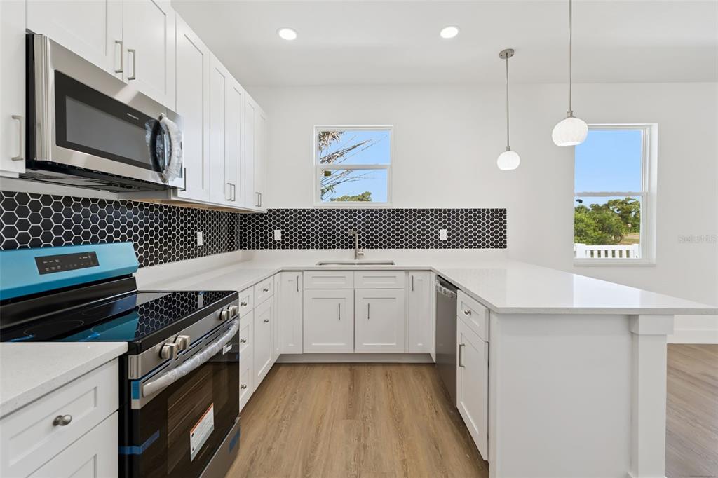 A kitchen features white cabinets, a black honeycomb tile backsplash, and a stainless steel stove — 2713 SAN LUIS ROAD, HOLIDAY, FL