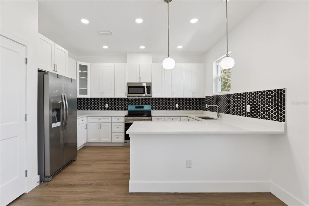 A modern kitchen features white cabinetry, stainless steel appliances, and a black hexagonal tile backsplash — 2713 SAN LUIS ROAD, HOLIDAY, FL