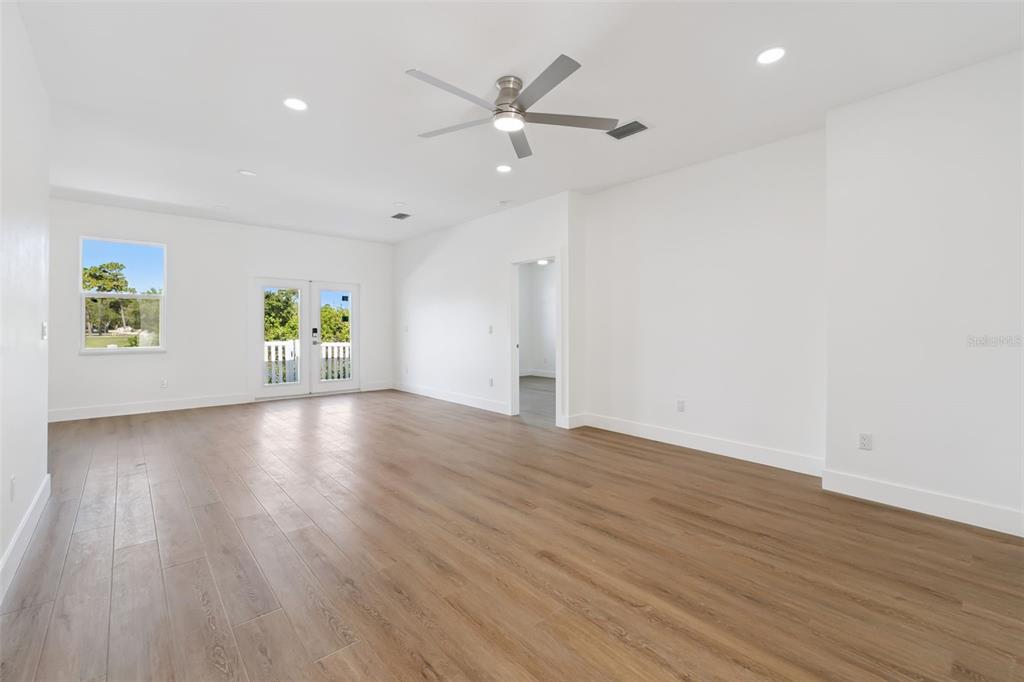 A bright, empty room features light wood-look flooring, white walls, a ceiling fan, and doors — 2713 SAN LUIS ROAD, HOLIDAY, FL