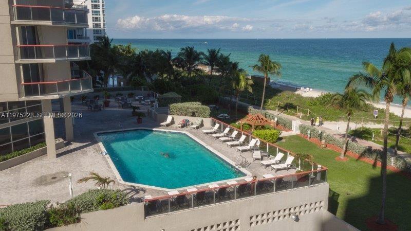 An elevated view of a swimming pool, patio furniture, and a beach with the ocean — 6767 Collins Ave # 706, Miami Beach FL 33141, MIAMI BEACH, FL
