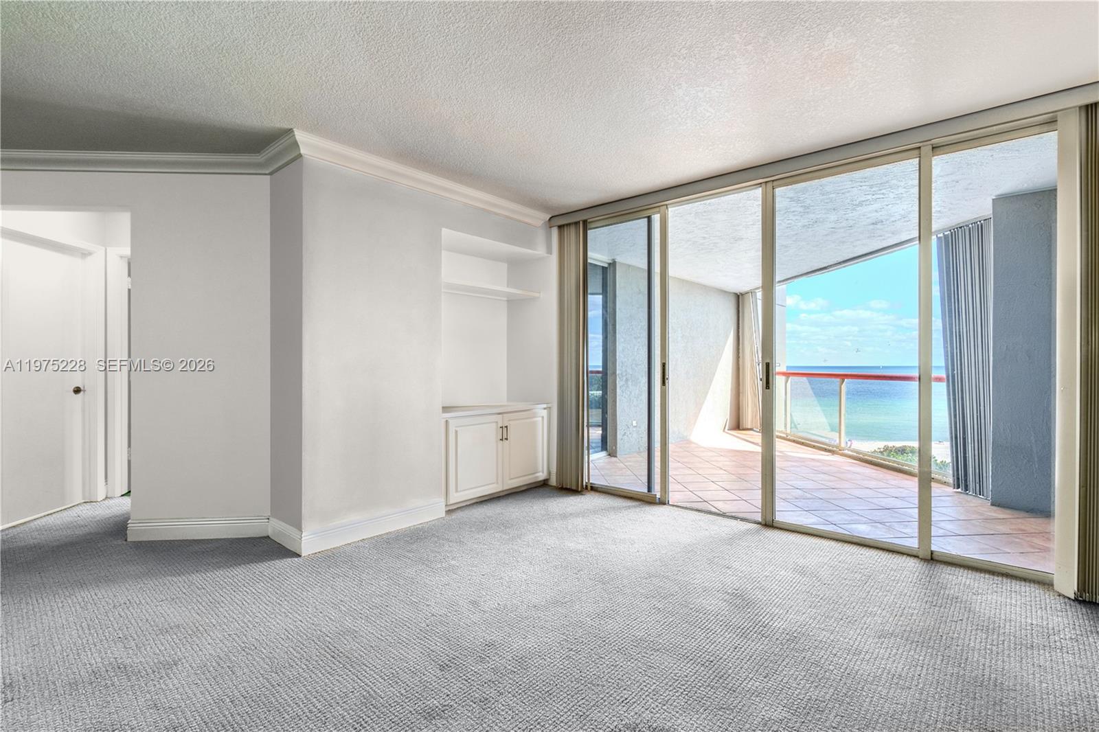 A carpeted room features built-in shelving and sliding glass doors opening to an oceanfront balcony — 6767 Collins Ave # 706, Miami Beach FL 33141, MIAMI BEACH, FL