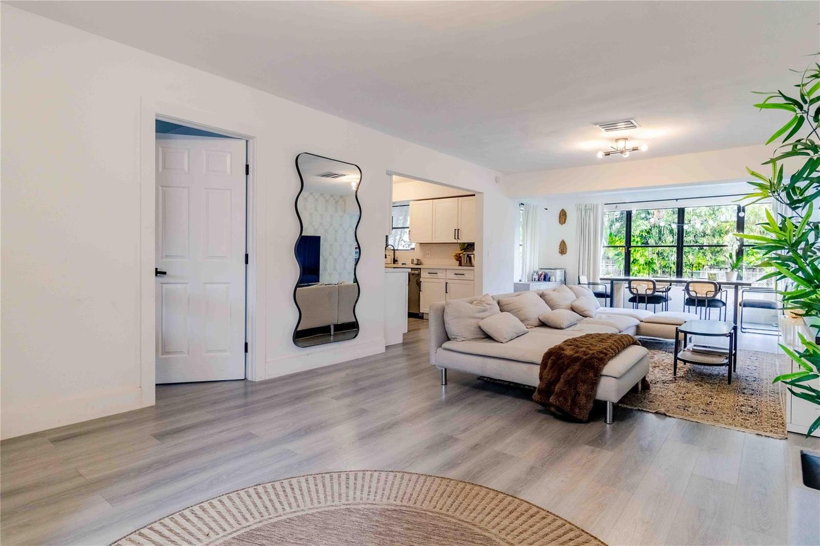 A living room with light wood-look flooring, a sectional sofa, and an adjacent kitchen area — 2515 NE 207th Street, Miami FL 33180, MIAMI, FL