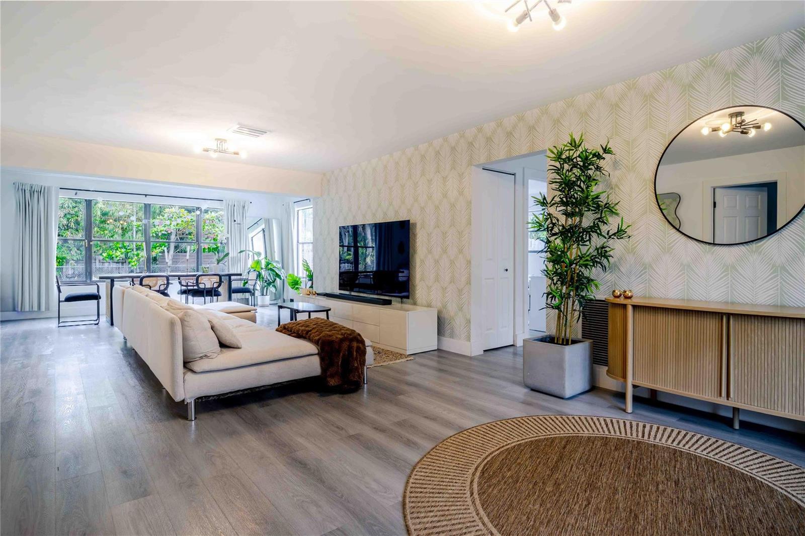 A living room features light wood flooring, patterned wallpaper, a large sofa, and a television — 2515 NE 207th Street, Miami FL 33180, MIAMI, FL
