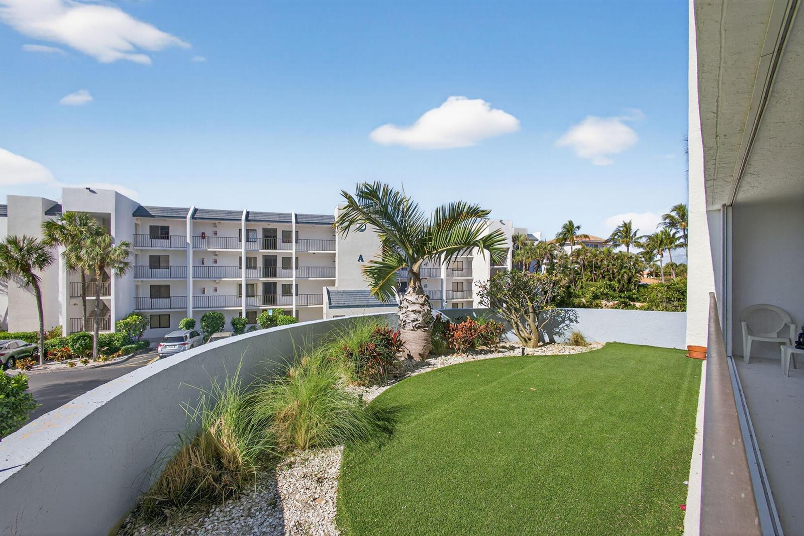 A balcony features artificial turf, a palm tree, and a view of an apartment building — 1300 S Highway A1a Highway # 119, Jupiter FL 33477, JUPITER, FL