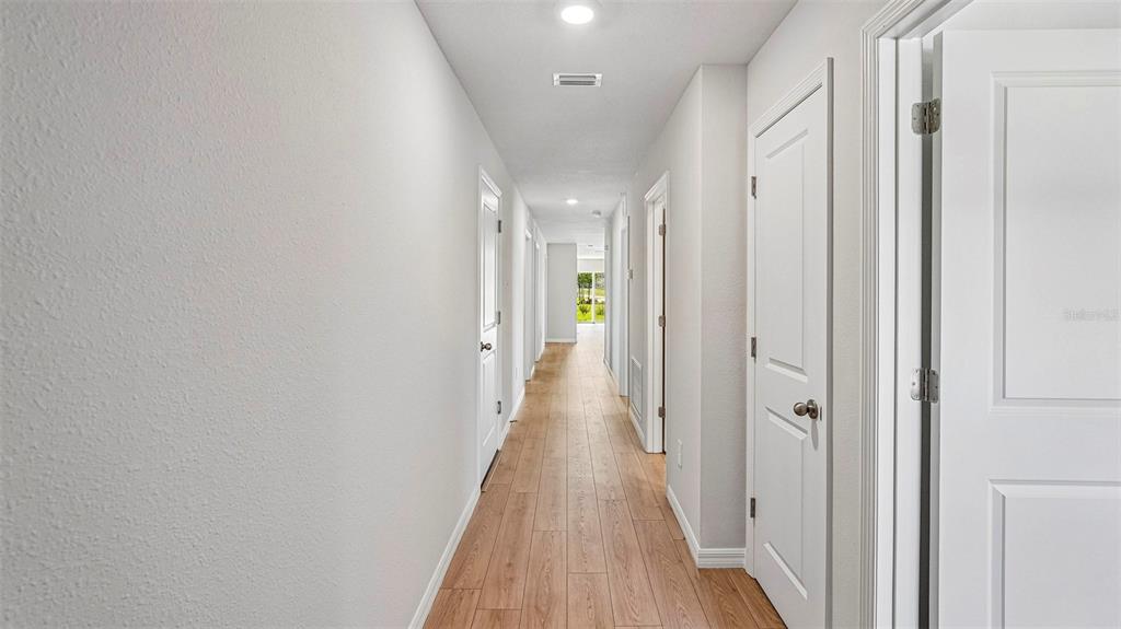 A long hallway with light wood-look flooring and white doors leads toward a bright opening — 10420 CURVING CREEK LOOP, PARRISH, FL