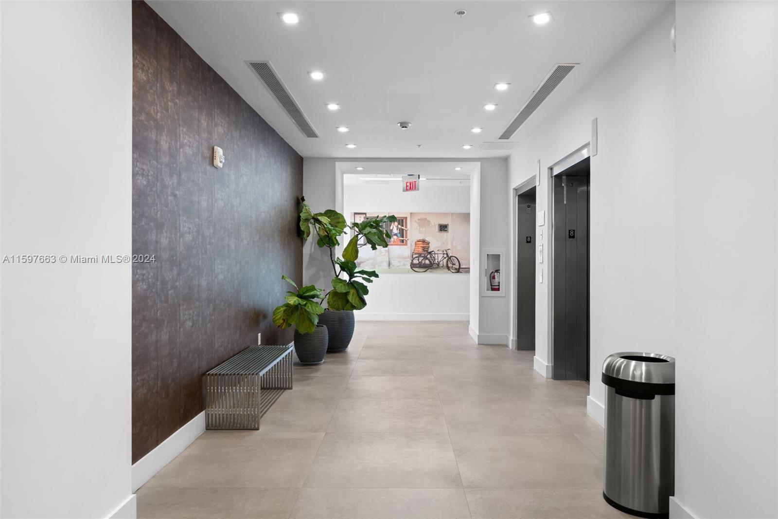 A modern building hallway features a dark textured accent wall, two elevators, and potted plants — 800 SE 4th Ave # 817, Hallandale Beach FL 33009, HALLANDALE BEACH, FL