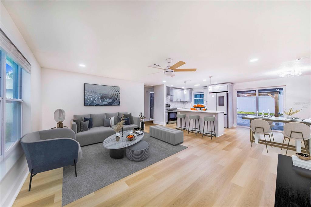 An open-concept living room and kitchen featuring light wood floors, a gray sofa, and island — 3104 ASH COURT, DUNEDIN, FL