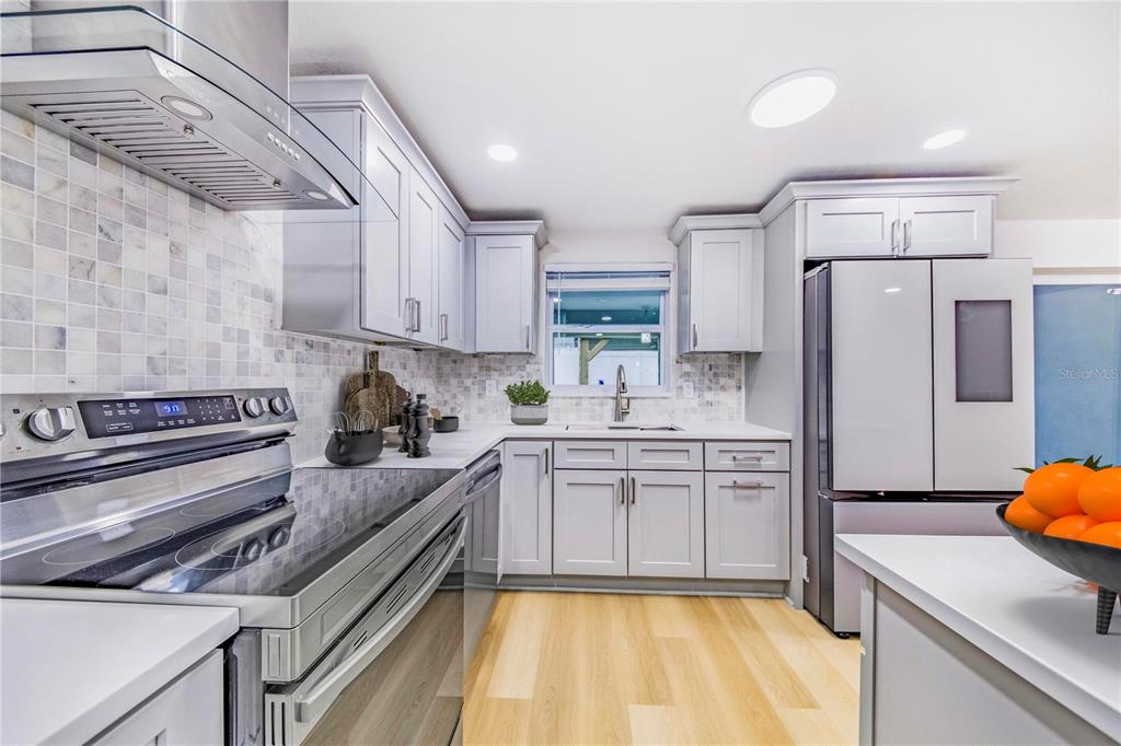 A modern kitchen features light gray cabinets, stainless steel appliances, and light wood-look flooring — 3104 ASH COURT, DUNEDIN, FL