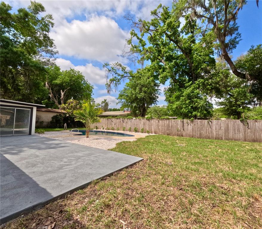 A backyard features a concrete patio, a small swimming pool, and a wooden privacy fence — 1103 N PENNSYLVANIA AVENUE, PLANT CITY, FL