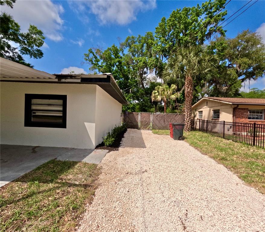 A gravel driveway leads toward a fenced backyard between two residential houses — 1103 N PENNSYLVANIA AVENUE, PLANT CITY, FL