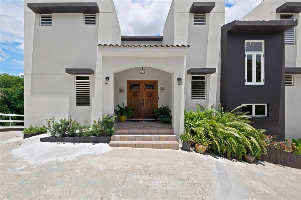 The exterior of a modern two-story house features a tiled entryway with double wooden doors — Lot-7 MAMEYES I, HACIENDA PANORAMA, LUQUILLO, PR