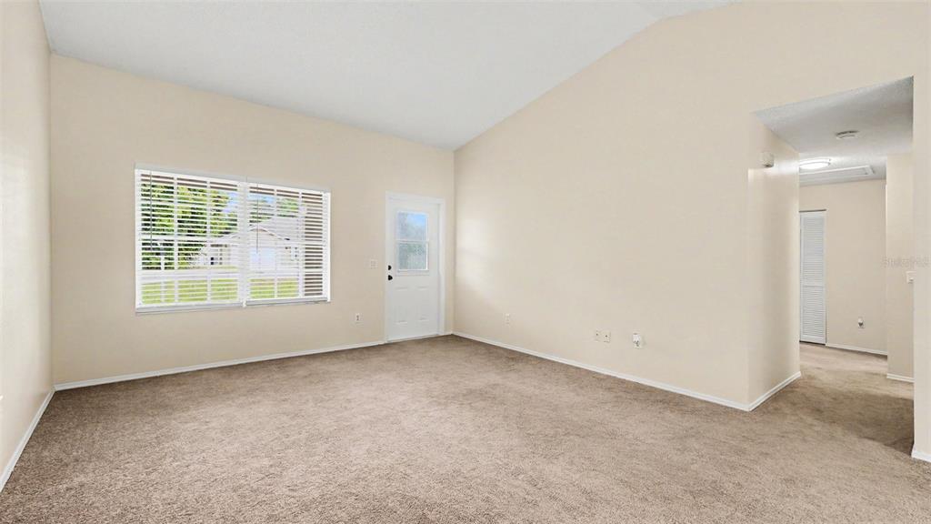 An empty living room features beige carpet, light-colored walls, a vaulted ceiling, and a door — 206 OAK CIRCLE, OCALA, FL