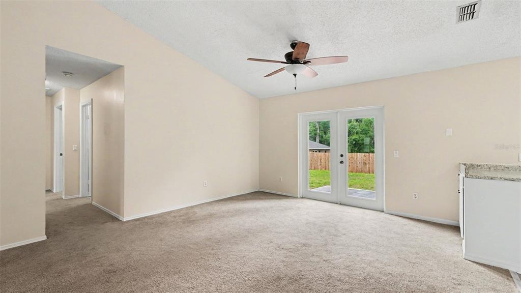 A carpeted living room features a vaulted ceiling, a ceiling fan, and glass patio doors — 206 OAK CIRCLE, OCALA, FL