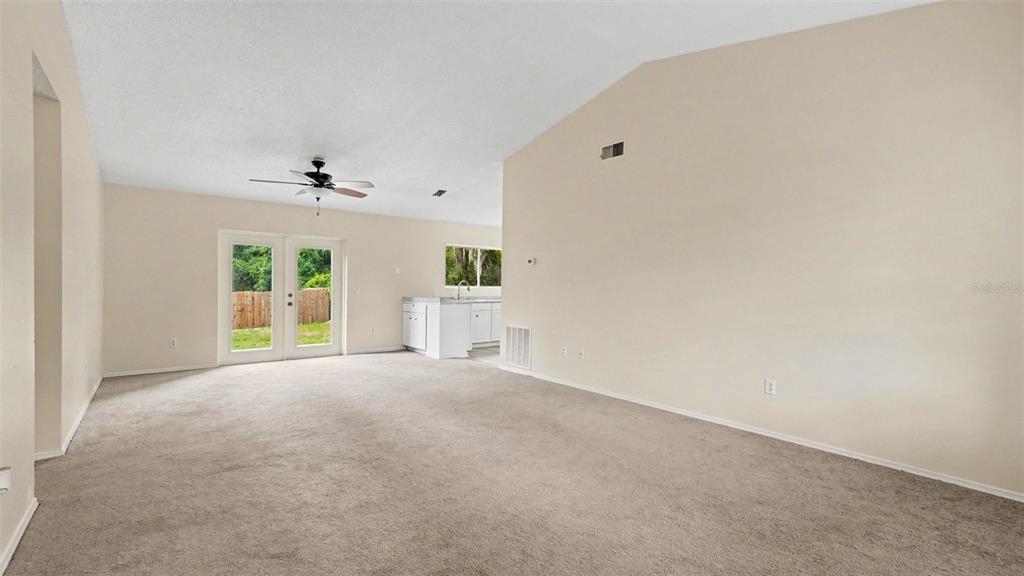 A spacious living room features beige carpeting, vaulted ceilings, a ceiling fan, and glass doors — 206 OAK CIRCLE, OCALA, FL