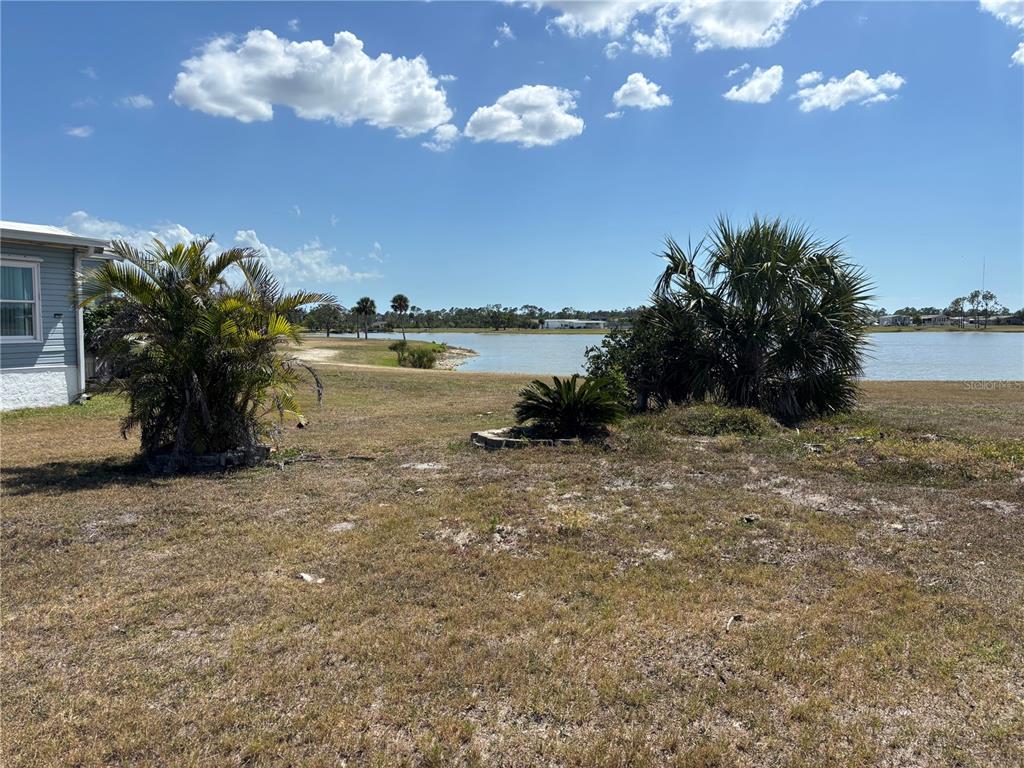 A grassy yard with palm trees overlooks a lake under a blue sky with clouds — 7357 ADANA AVENUE, PORT CHARLOTTE, FL