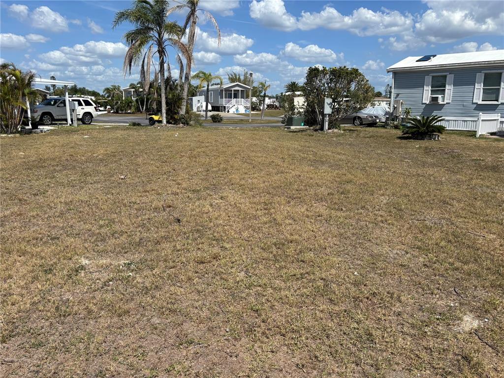 A vacant, grassy lot sits between two manufactured homes under a bright, cloudy sky — 7357 ADANA AVENUE, PORT CHARLOTTE, FL