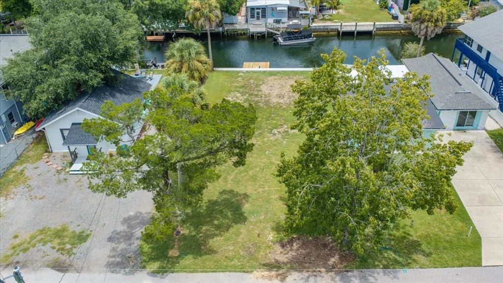 An aerial view shows a vacant grassy lot situated between two houses along a canal — 7250 COVENTRY COURT, SPRING HILL, FL