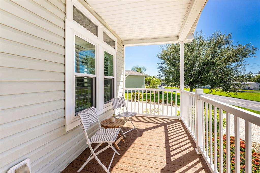 A covered porch features light-colored siding, a wooden deck, white railings, and two chairs — 24819 RIO VILLA LAKES CIRCLE, PUNTA GORDA, FL