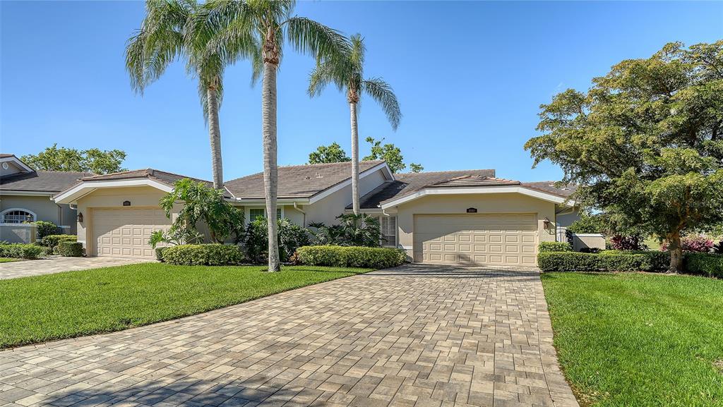 A single-story house features two garage doors, a paved driveway, and tall palm trees — 4060 PENSHURST PARK, SARASOTA, FL