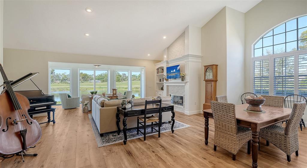 A living and dining area features wood flooring, a fireplace, and large windows overlooking water — 4060 PENSHURST PARK, SARASOTA, FL