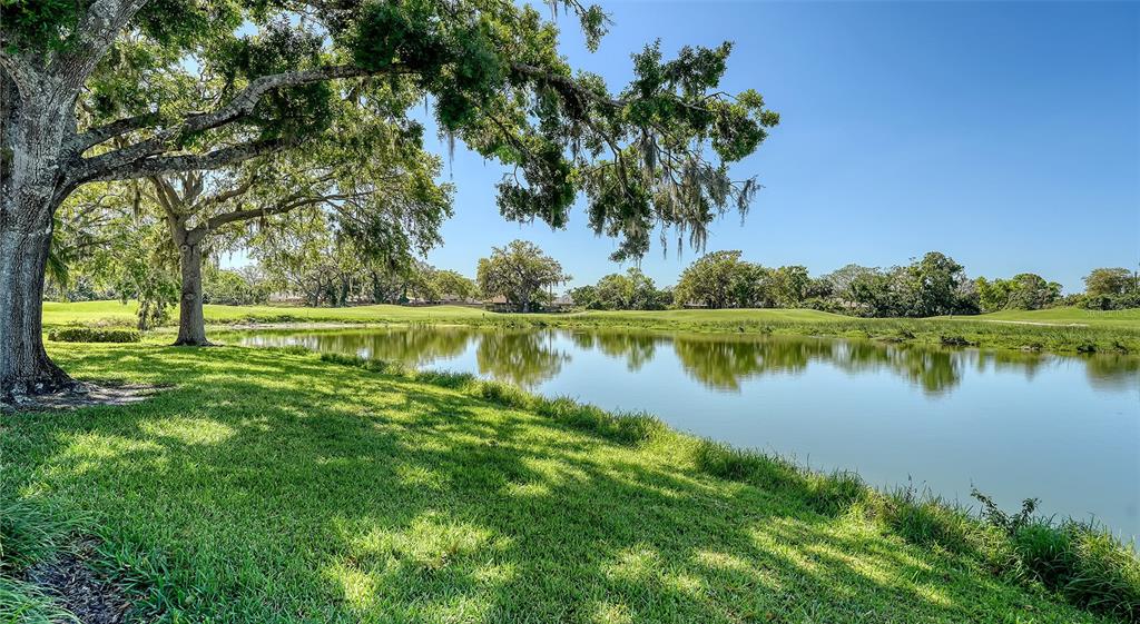 A large oak tree shades a grassy bank overlooking a calm pond on a golf course — 4060 PENSHURST PARK, SARASOTA, FL