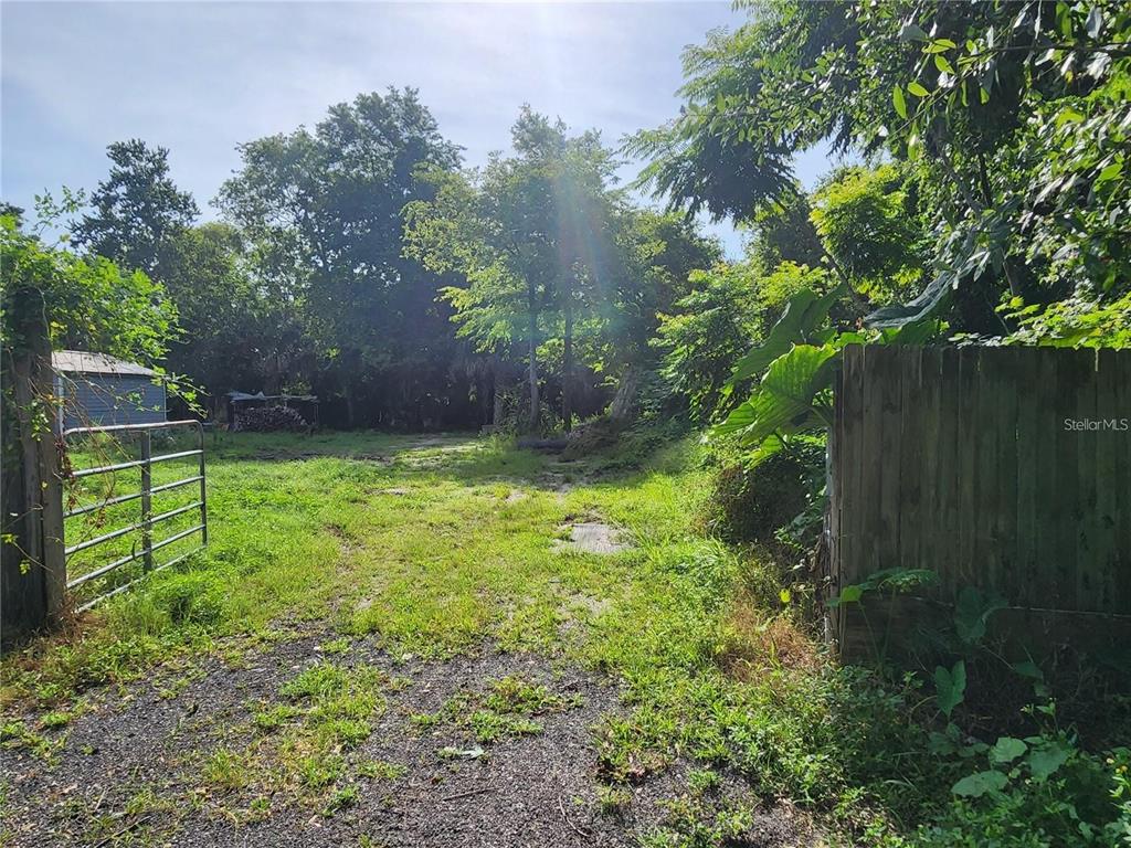 A gravel driveway leads through a metal gate toward a wooded area with a shed — SANFORD AVENUE, SANFORD, FL