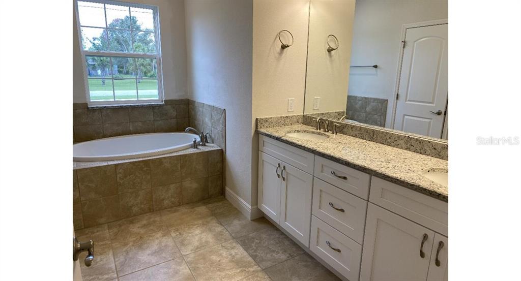 A bathroom features a soaking tub with tile surround, a granite-topped vanity, and tile flooring — 3843 SAN MATEO DRIVE, NORTH PORT, FL