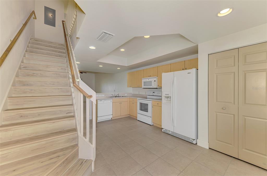 A kitchen with light wood cabinets and white appliances sits beside a staircase with wood-look steps — 1246 RIO DE JANEIRO AVENUE UNIT 510, PUNTA GORDA, FL
