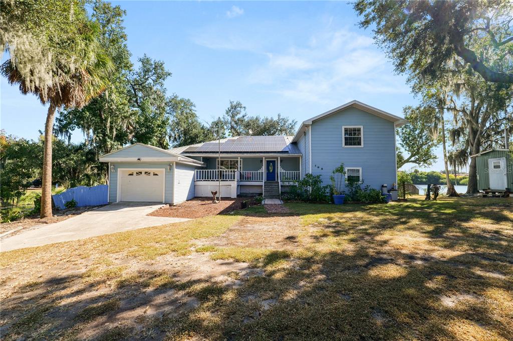 A two-story light blue house with a garage and solar panels sits on a lawn — 109 NE 4TH AVENUE, MULBERRY, FL