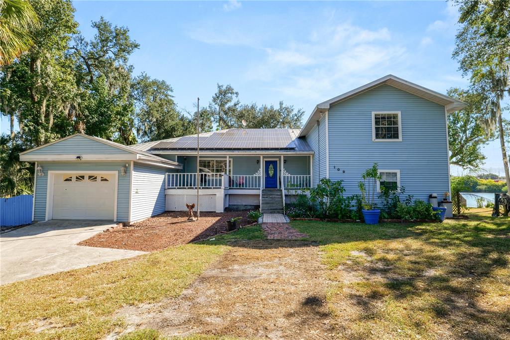 An aerial view of a light blue house nestled among trees on a lakefront lot — 109 NE 4TH AVENUE, MULBERRY, FL