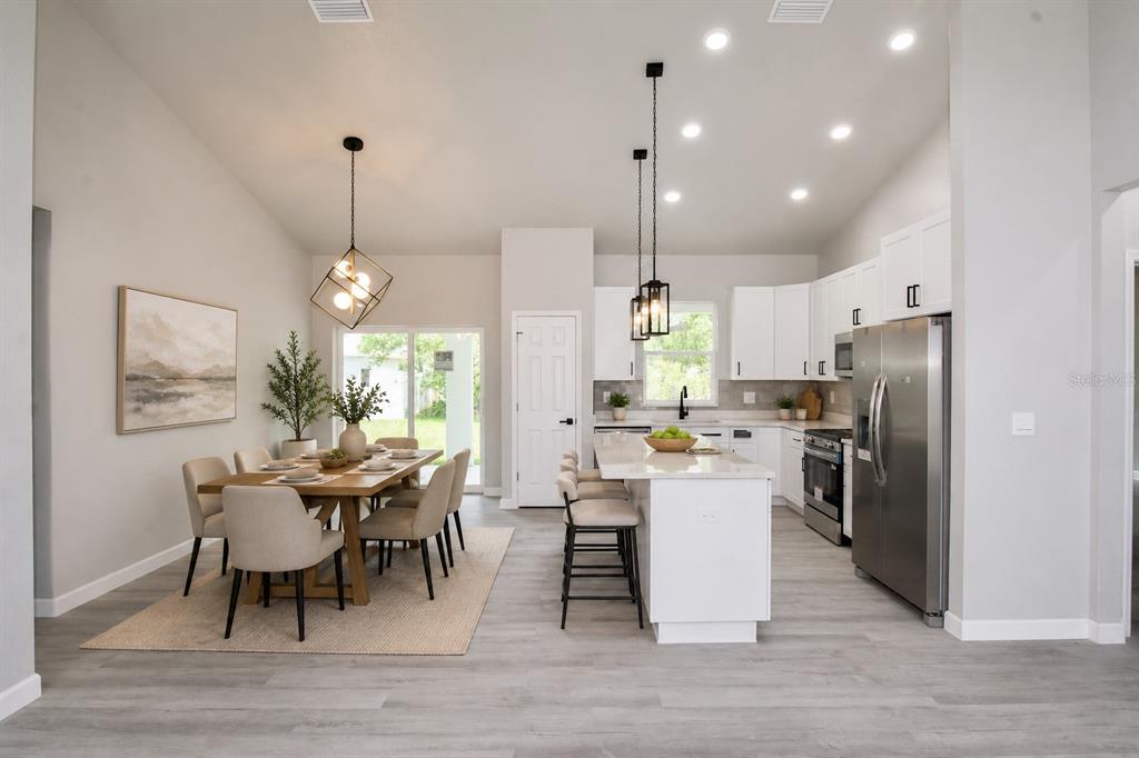 A modern open-concept kitchen and dining area with white cabinetry, stainless appliances, and wood flooring — 4608 CORTEZ BOULEVARD, SEBRING, FL