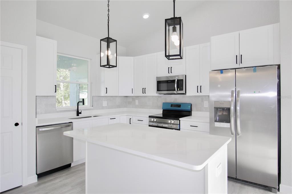 A modern kitchen features white cabinets, stainless steel appliances, a white island, and pendant lighting — 4608 CORTEZ BOULEVARD, SEBRING, FL