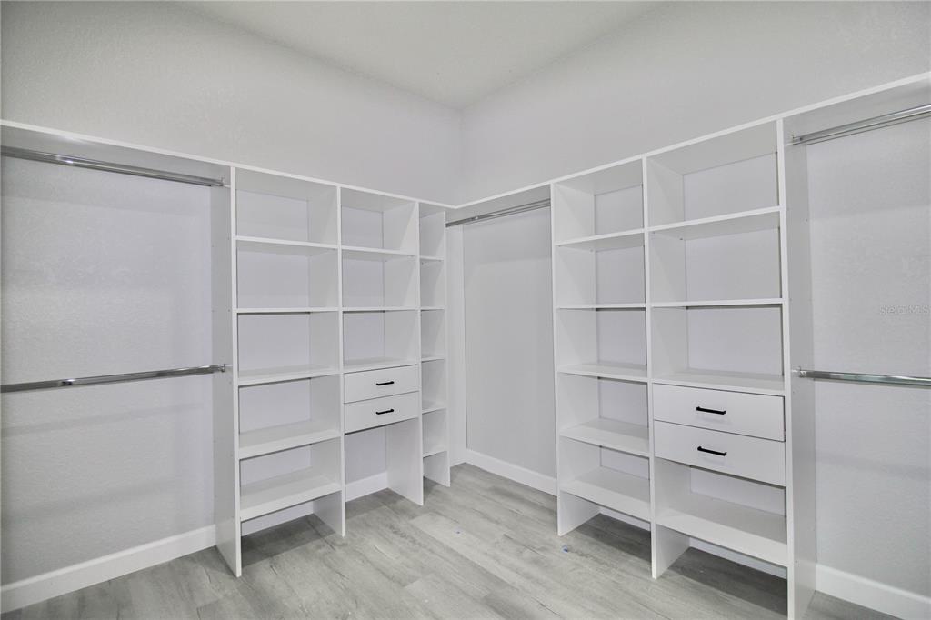 A walk-in closet features white shelving units, hanging rods, and light-colored wood-look flooring — 4608 CORTEZ BOULEVARD, SEBRING, FL