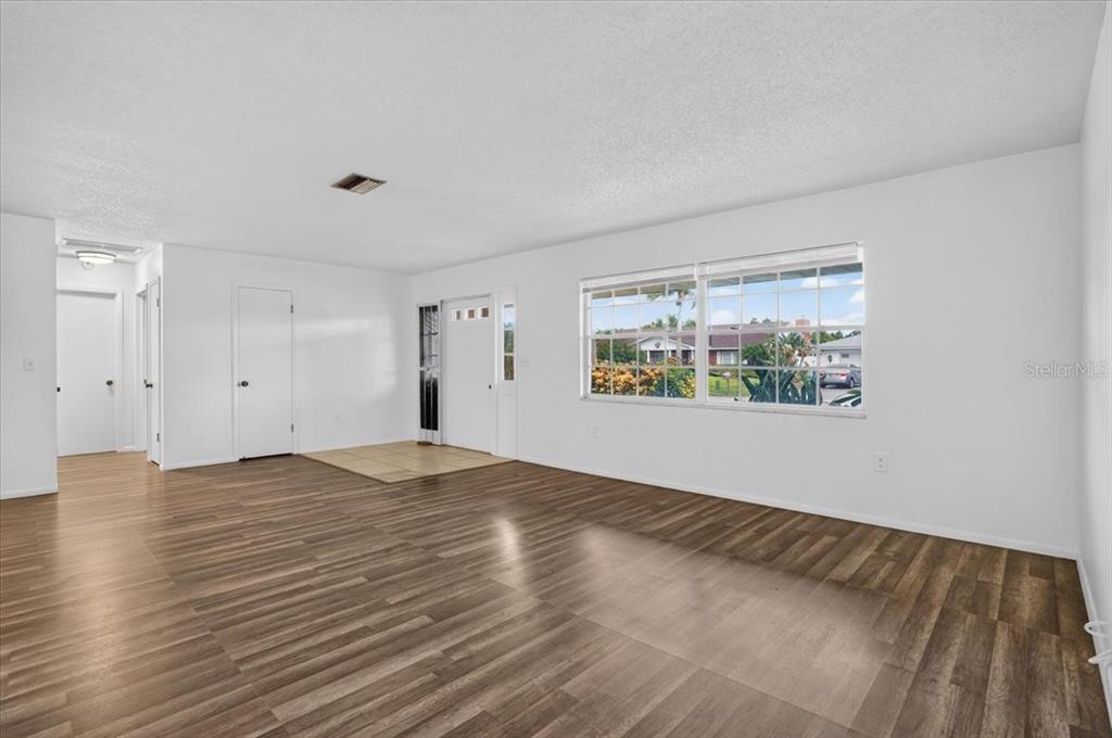 A bright living room features wood-look flooring, white walls, and a large window — 6814 16TH AVENUE DRIVE W, BRADENTON, FL