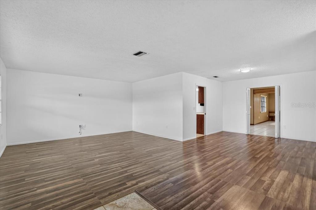 An empty room with white walls and wood-look flooring features a doorway to another room — 6814 16TH AVENUE DRIVE W, BRADENTON, FL