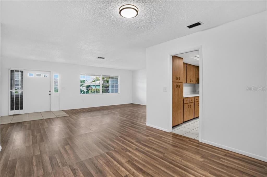 A bright living room with wood-look flooring leads into a kitchen with wooden cabinets — 6814 16TH AVENUE DRIVE W, BRADENTON, FL