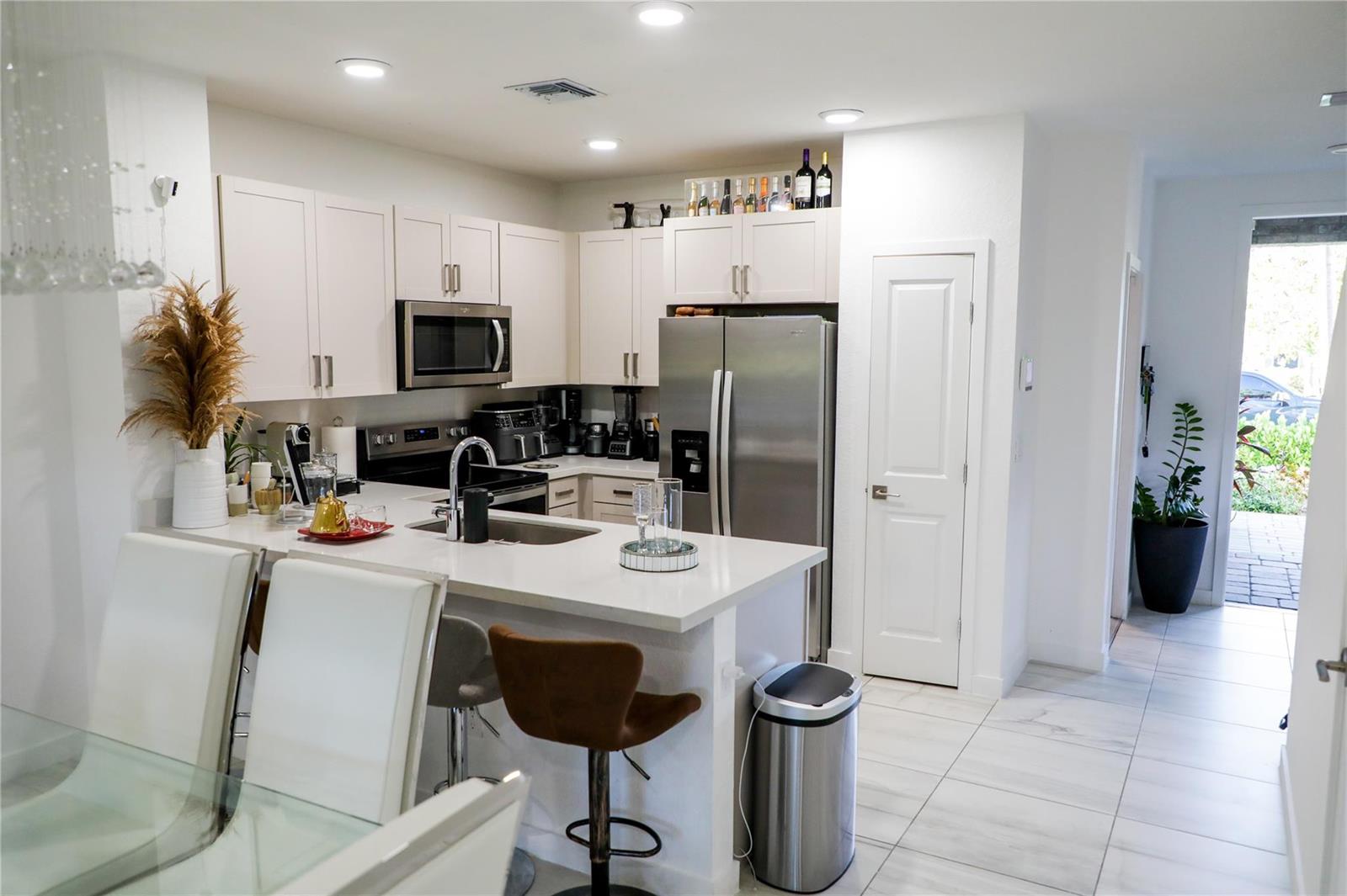 A modern kitchen features white cabinetry, stainless steel appliances, a breakfast bar, and tile flooring — 148 SE 5th Court, Deerfield Beach FL 33441, DEERFIELD BEACH, FL