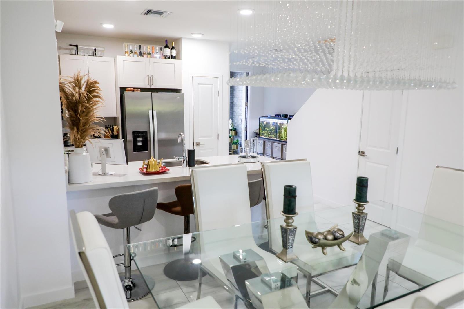 A modern kitchen with white cabinetry and a glass dining table in the foreground — 148 SE 5th Court, Deerfield Beach FL 33441, DEERFIELD BEACH, FL