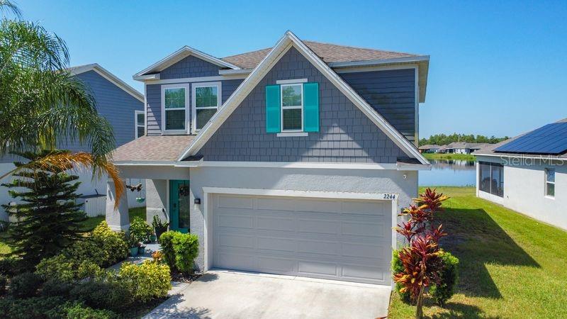 A two-story suburban house with a gray garage, blue shutters, and a nearby pond — 2244 CANYON BREEZE AVENUE, KISSIMMEE, FL