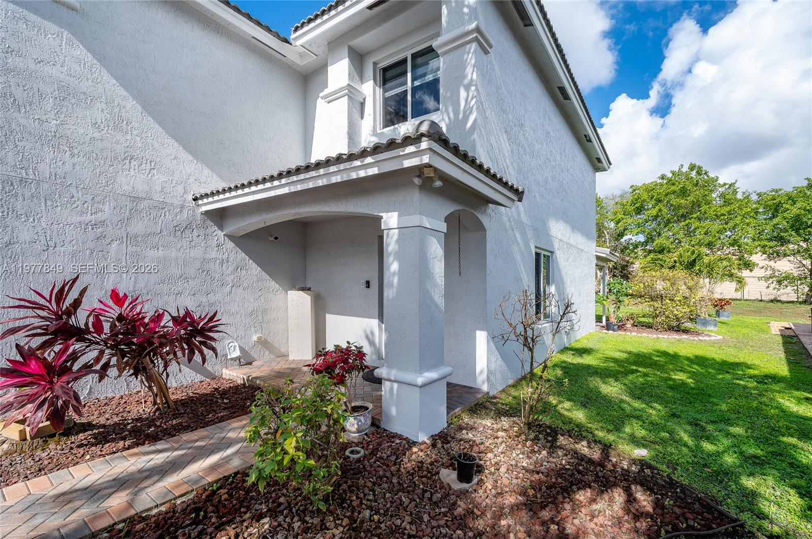 The exterior of a two-story white stucco house features a covered entryway and landscaped yard — 13391 SW 42nd St, Miramar FL 33027, MIRAMAR, FL