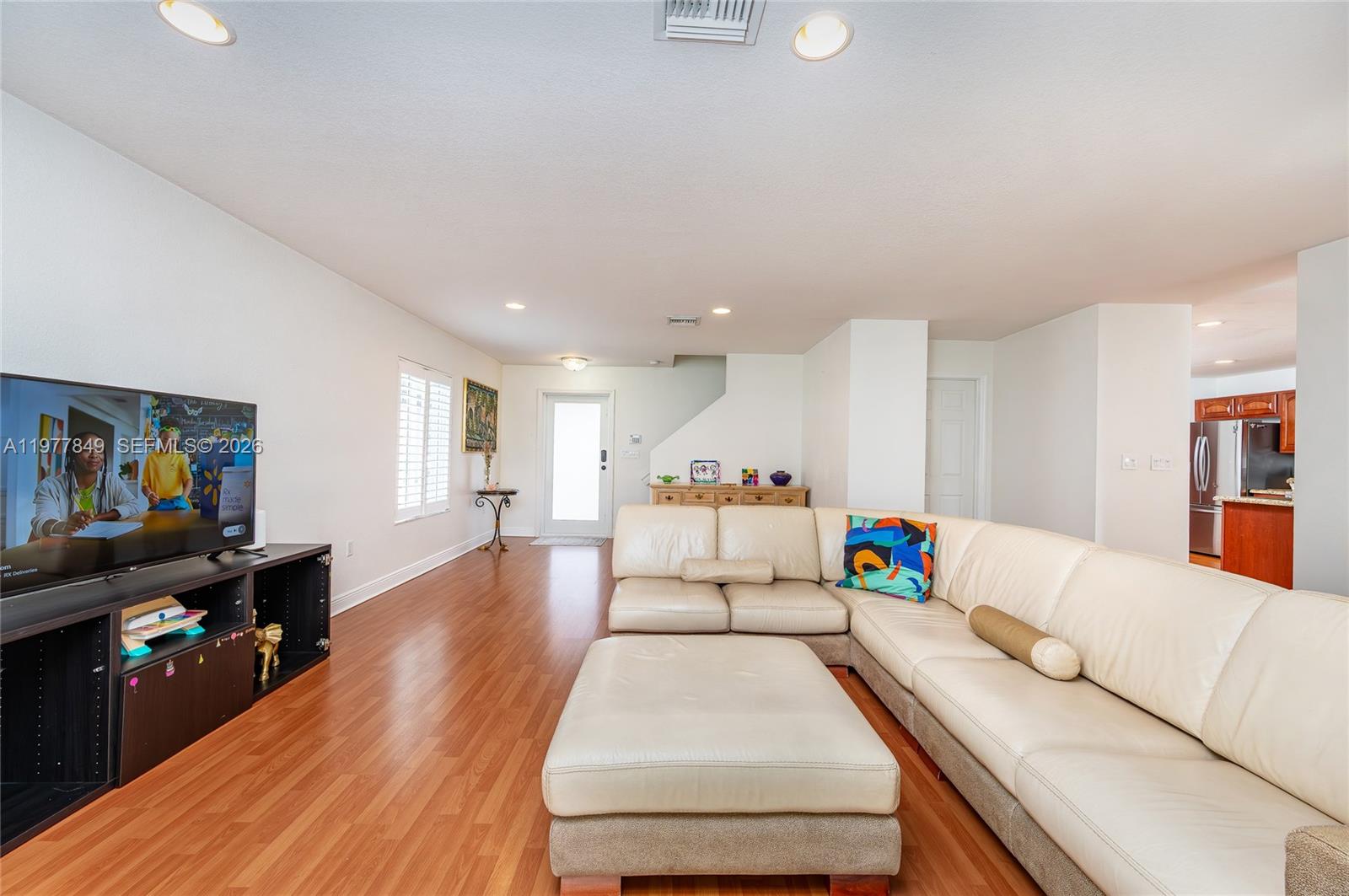 A living room features a large white sectional sofa, a television on a black stand, and wood flooring — 13391 SW 42nd St, Miramar FL 33027, MIRAMAR, FL