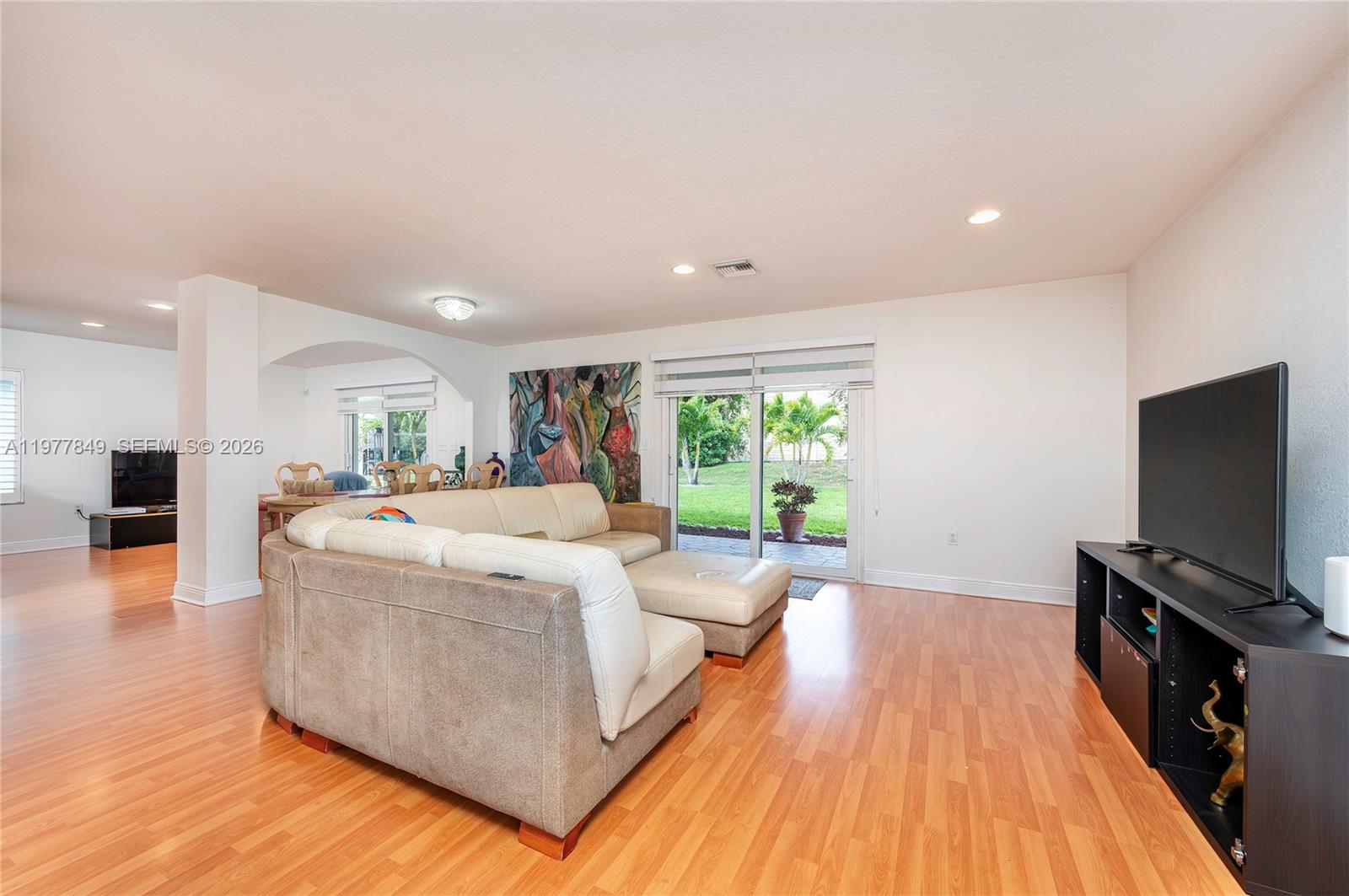A living room features light wood flooring, a sectional sofa, a television, and sliding glass doors — 13391 SW 42nd St, Miramar FL 33027, MIRAMAR, FL