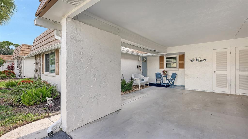 A white stucco house features a covered carport, a small patio area, and landscaped gardens — 2623 RIVERBLUFF PARKWAY UNIT V144, SARASOTA, FL