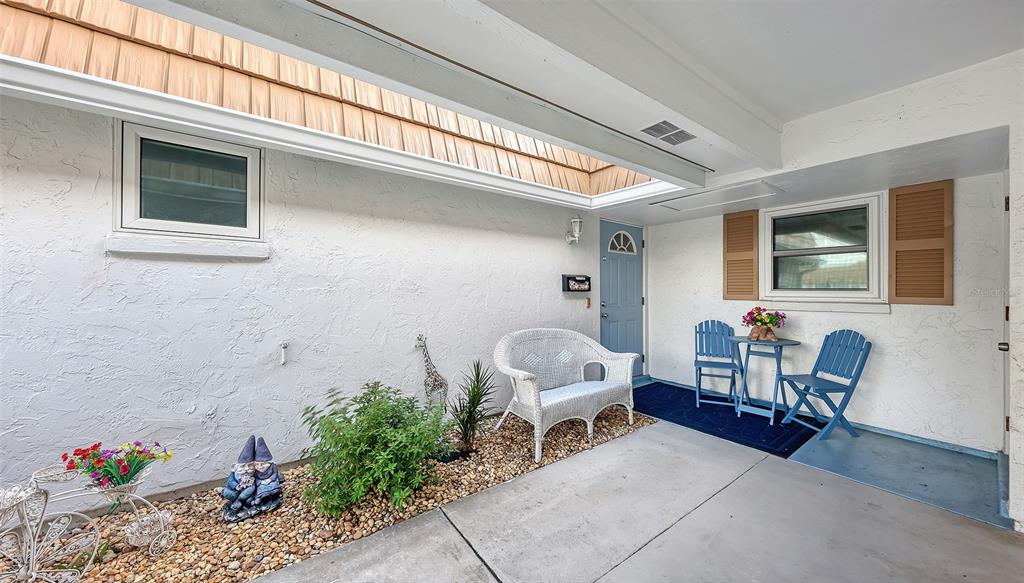 A covered patio features a white wicker bench, blue chairs, and a small table — 2623 RIVERBLUFF PARKWAY UNIT V144, SARASOTA, FL