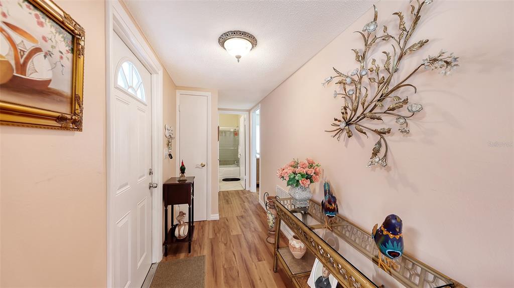 A hallway features wood-look flooring, a decorative metal wall sculpture, and a console table — 2623 RIVERBLUFF PARKWAY UNIT V144, SARASOTA, FL