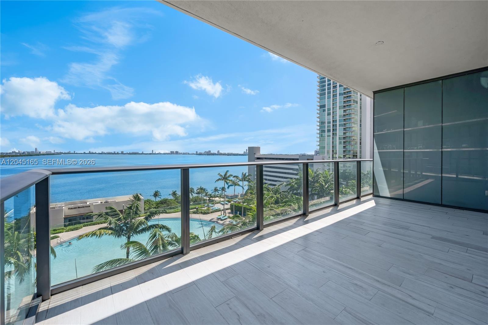 A balcony with glass railings overlooks a swimming pool, palm trees, and the ocean — 480 NE 31st St # 907, Miami FL 33137, MIAMI, FL