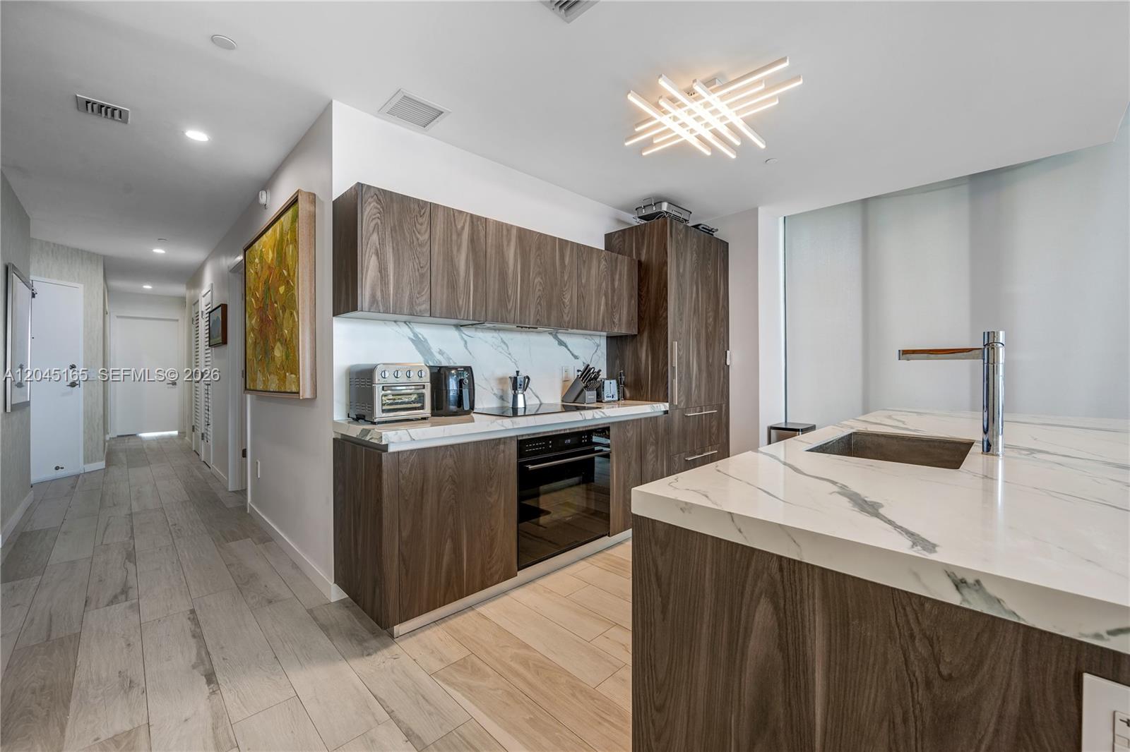A modern kitchen features wood-grain cabinets, marble countertops, and a contemporary light fixture — 480 NE 31st St # 907, Miami FL 33137, MIAMI, FL
