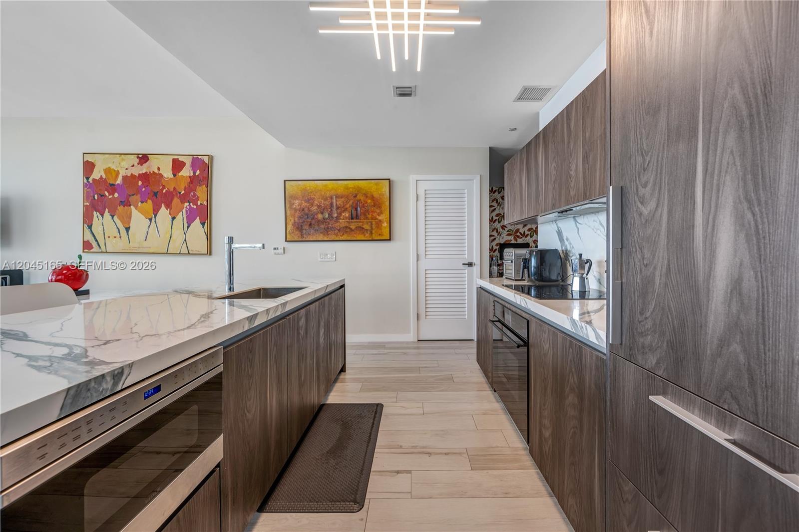 A modern kitchen features dark wood cabinetry, marble countertops, and a unique geometric ceiling light — 480 NE 31st St # 907, Miami FL 33137, MIAMI, FL