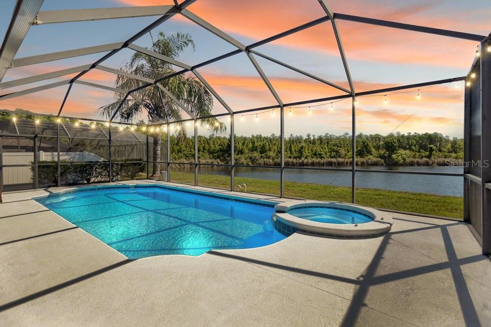 A screened-in pool and spa overlook a lake at sunset — 8758 CRYSTAL CREEK COURT, LAND O LAKES, FL